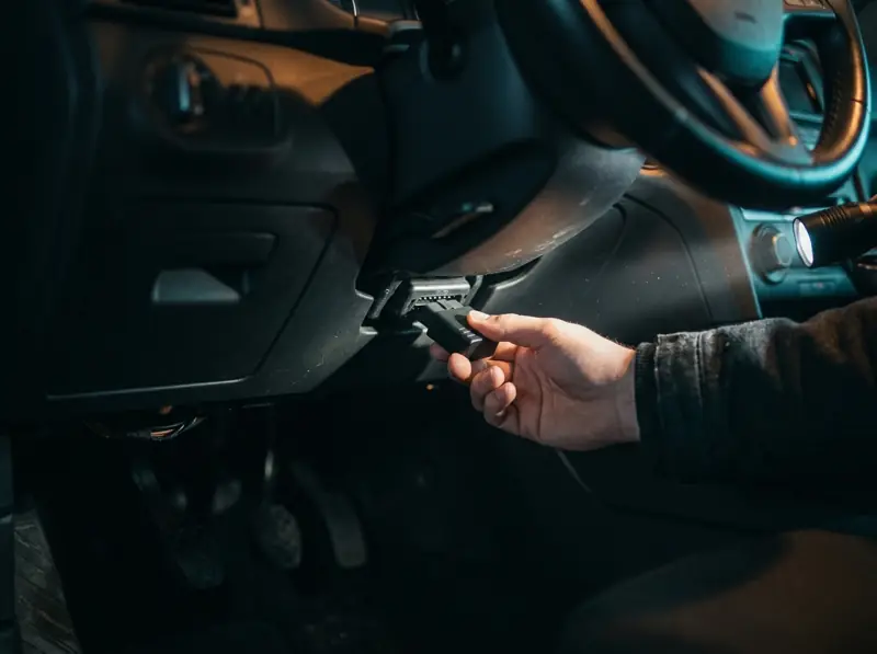 Mano conectando un adaptador OBD2 sin marca al puerto de 16 pines bajo el volante