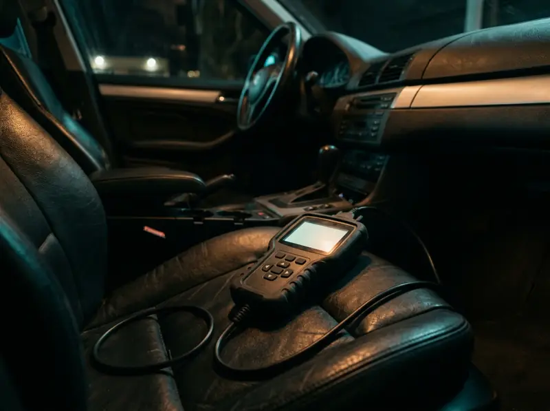 Escáner de mano con pantalla sobre un asiento de cuero, con el cable hacia el tablero